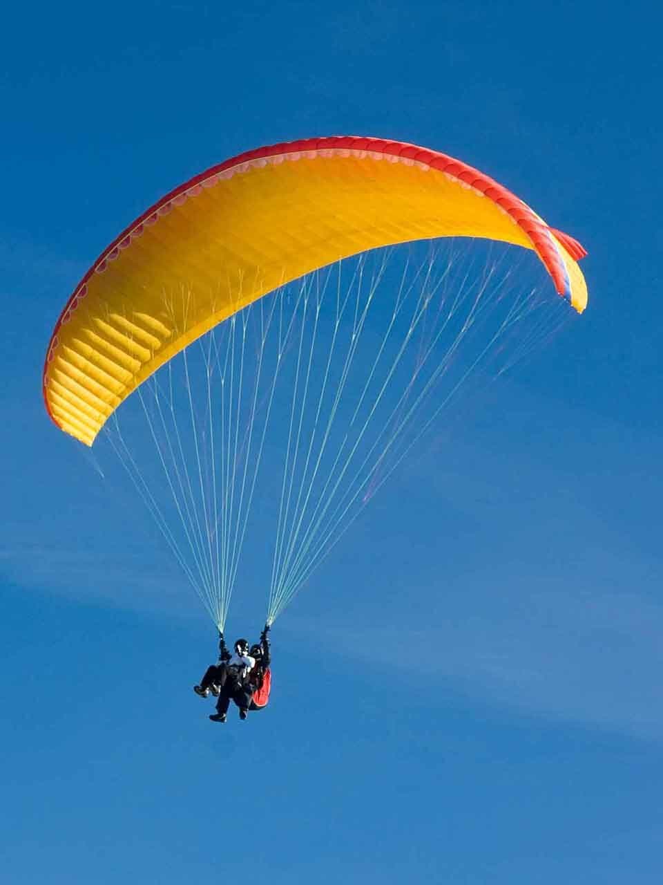 Parapente amarelo em voo duplo, visto de baixo